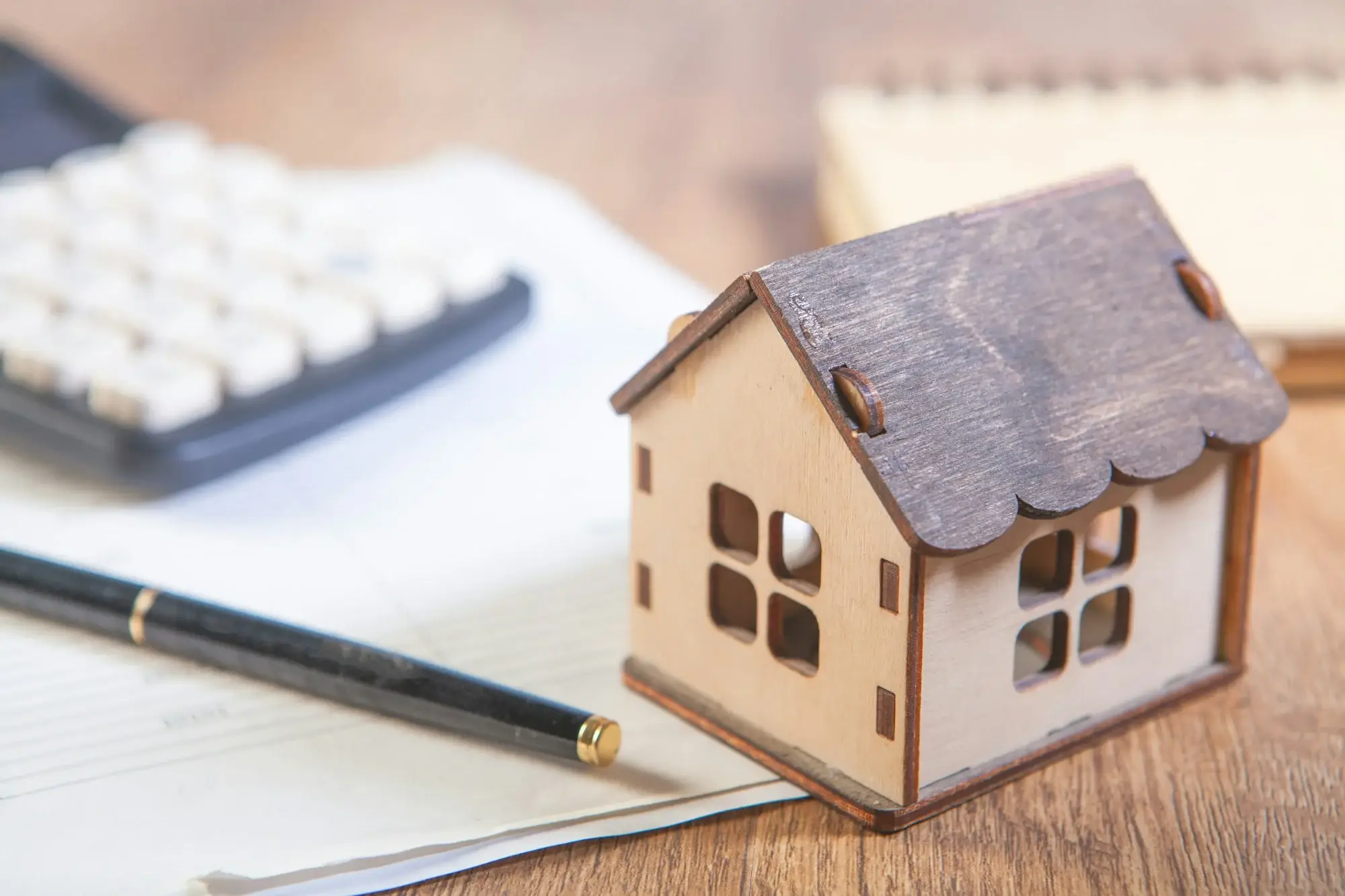 Casa en miniatura junto a una calculadora, símbolo de las deudas del hogar